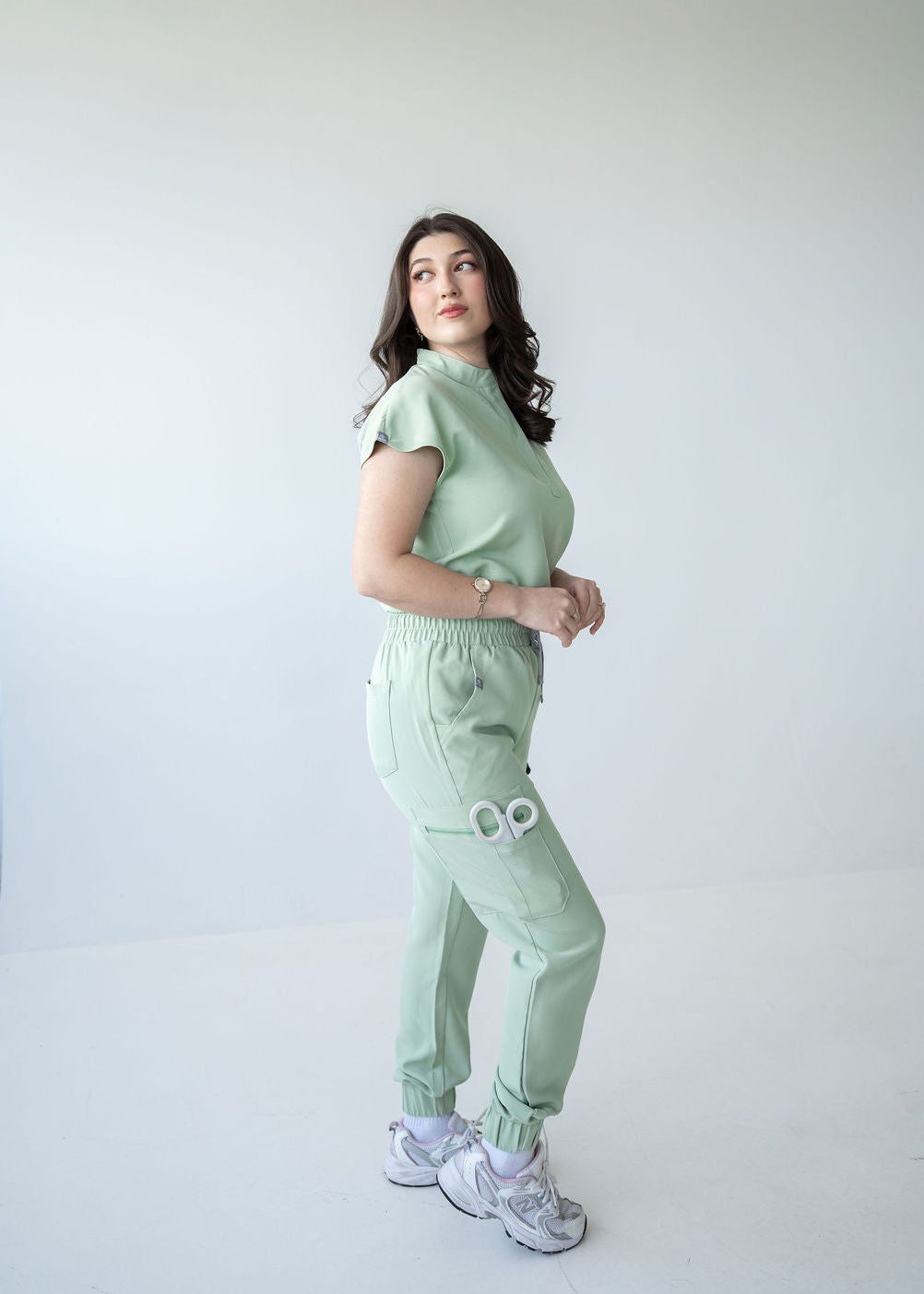 Woman wearing  mint green scrubs against a white background